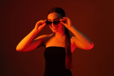 Güneş gözlüklü, arka planda, neon ışıklı güzel bir genç kadının portresi.