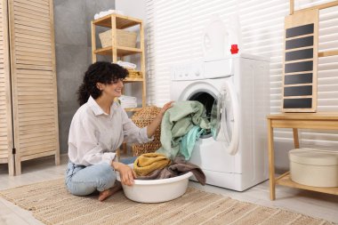 Çamaşır makinesinden çamaşırları çıkaran kadın.