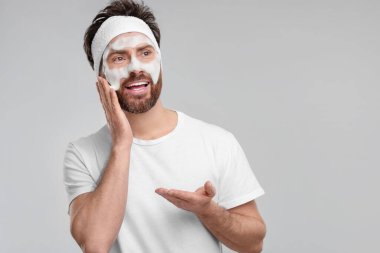 Saçbandı olan adam yüzünü açık gri arka planda yıkıyor, mesaj için yer var.