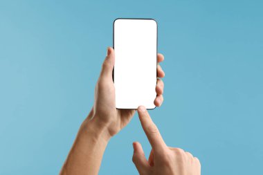 Açık mavi arka planda boş ekranlı akıllı telefon kullanan adam, yakın plan. Tasarım için model