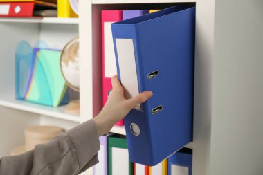 İçerideki raflardan klasör ofis klasörünü alan kadın.