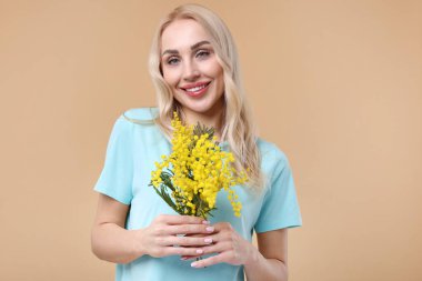 Bej arka planda güzel bir buketi olan mutlu genç bir kadın.