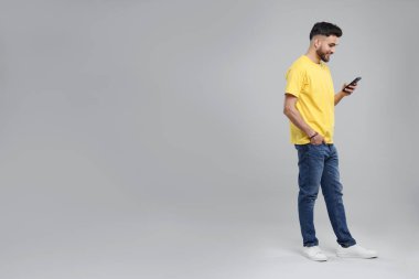 Gri arkaplanda akıllı telefon kullanan yakışıklı genç adam, metin için boşluk