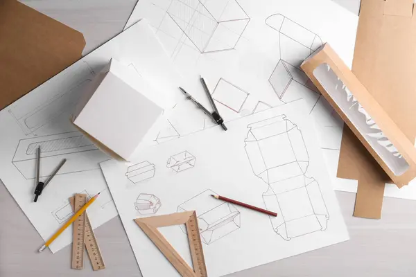Creating packaging design. Drawings, boxes and stationery on light wooden table, flat lay