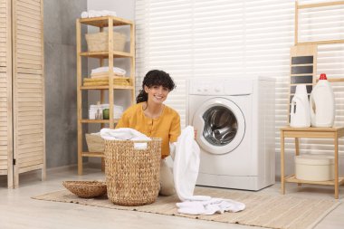 Çamaşır makinesinin yanında çamaşırları olan mutlu kadın.