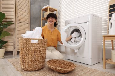 Çamaşır makinesine çamaşır koyan mutlu bir kadın.