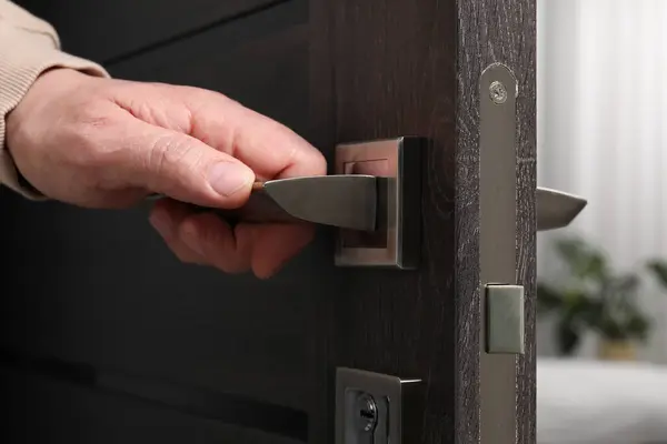 Man opening wooden door indoors, closeup of hand on handle