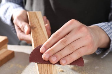 Gri masadaki zımpara kağıdıyla ahşap tahtayı cilalayan adam, yakın plan.