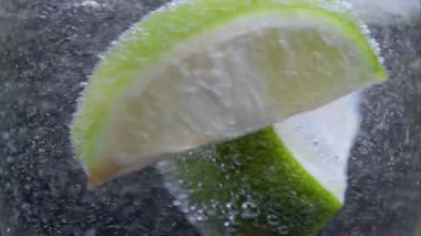 Işıl ışıl suda dönen iki kireç ve buz kübü, camın yakın görüntüsü.