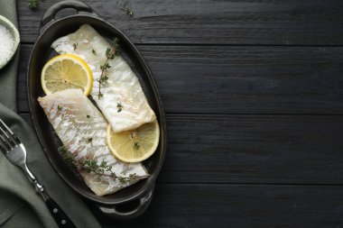 Kekik ve limonlu taze çiğ morina filetosu siyah ahşap masada, düz yerde. Metin için boşluk