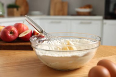 Yemek pişirme süreci. Metal çırpma, kase, un, yumurta ve elma mutfaktaki ahşap masada, yakın plan.