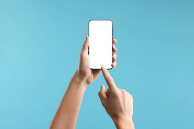 Açık mavi arka planda boş ekranlı akıllı telefon kullanan adam, yakın plan. Tasarım için model