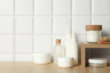 Farklı banyo aksesuarları ve ahşap masada beyaz fayanslı duvarın yanında kişisel bakım ürünleri, metin için yer