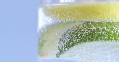 Limon dilimleri ve limon dilimleri köpüklü suda, açık mavi arkaplanda camın yakın görüntüsü