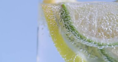 Limon ve limon köpüklü suda dilimler, açık mavi arka planda camın yakın görüntüsü