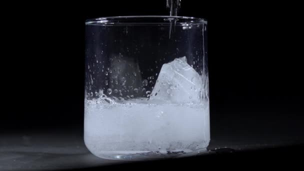 Häll Glittrande Vatten Glas Med Isbitar Mot Svart Bakgrund — Stockvideo
