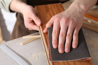 Gri masadaki zımpara kağıdıyla ahşap tahtayı cilalayan adam, yakın plan.