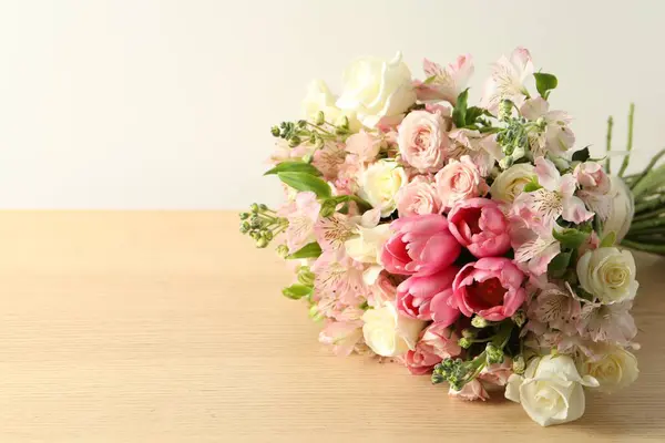 Beautiful bouquet of fresh flowers on wooden table near light wall. Space for text