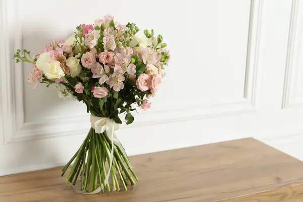 Beautiful bouquet of fresh flowers on wooden table near white wall, space for text