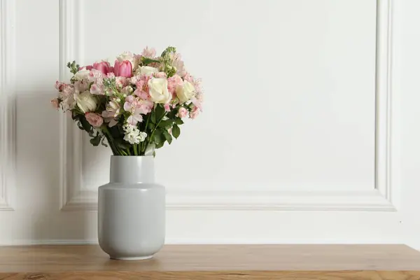 Beautiful bouquet of fresh flowers in vase on wooden table near white wall, space for text