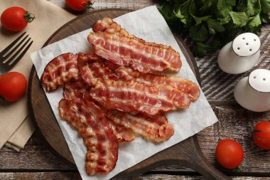 Kızarmış pastırma dilimleri, domatesler, maydanoz ve baharatlar ahşap kırsal masada, düz yerde.