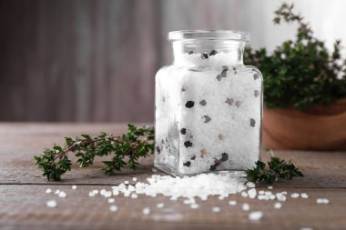 Cam kavanozda biberli tuz ve ahşap masada kekik.