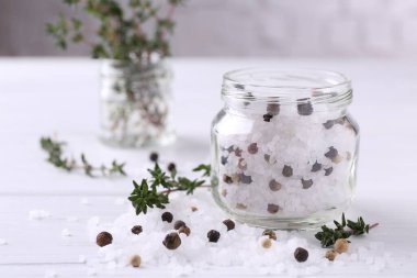 Cam kavanozda biberli tuz ve beyaz ahşap masada kekik, yakın plan.