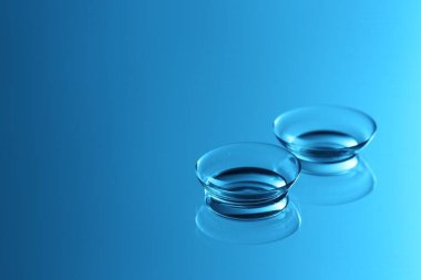 Ayna yüzeyinde bir çift kontakt lens, mavi tonda. Metin için boşluk