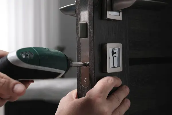 Handyman with electric screwdriver repairing door handle indoors, closeup