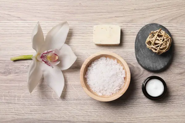 Flat lay composition with spa products and beautiful flower on light wooden table