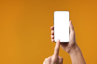 Turuncu arka planda boş ekranlı akıllı telefon kullanan adam, yakın plan. Tasarım için model