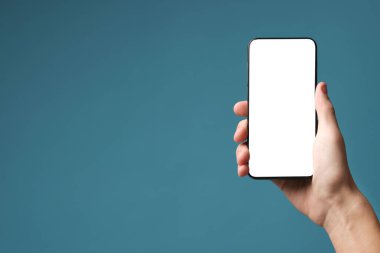 Açık mavi arka planda boş ekranlı akıllı telefon tutan adam, yakın plan. Tasarım için model
