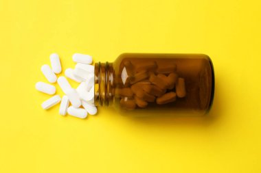 Sarı arka planda vitamin hapları ve şişe, üst manzara.