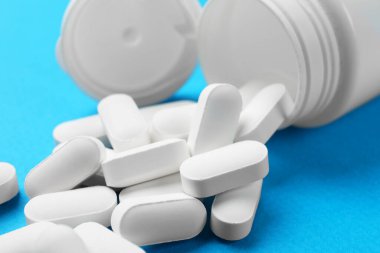 Açık mavi arka planda vitamin hapları ve şişe, yakın plan.