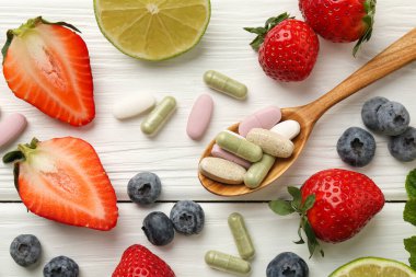 Farklı vitamin hapları ve beyaz ahşap masada taze meyveler.
