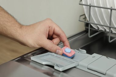 Deterjan tabletini açık bulaşık makinesine koyan adam, yakın plan.