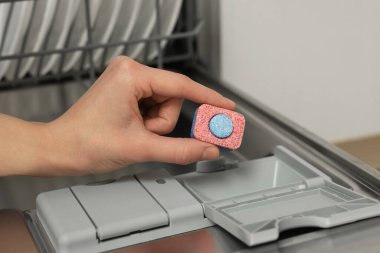 Kadın bulaşık makinesine deterjan koyuyor, yakın plan.