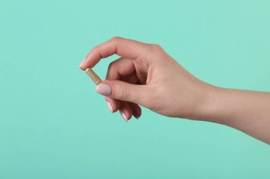 Turkuaz arka planda vitamin kapsülü tutan kadın, yakın plan. Sağlık takviyesi