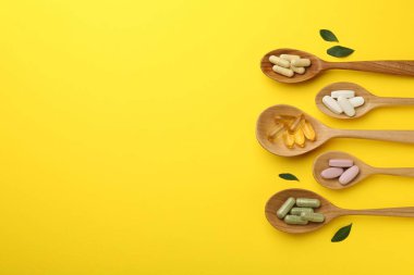 Kaşık içinde farklı vitamin hapları ve sarı arka planda yeşil yapraklar. Metin için boşluk