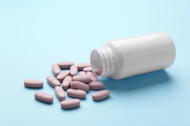 Açık mavi arka planda vitamin hapları ve şişe, yakın plan.