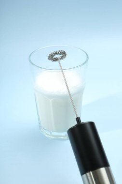 Mini mixer (milk frother) and whipped milk in glass on light blue background clipart