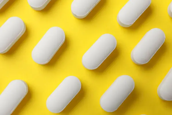 Vitamin pills on yellow background, flat lay