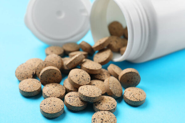 Bottle and vitamin pills on light blue background, closeup