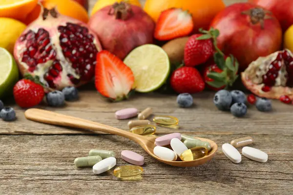 Different vitamin pills and fresh fruits on wooden table