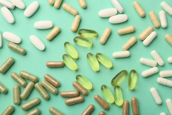 Different vitamin capsules on turquoise background, top view