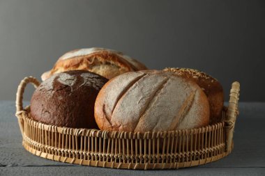 Gri ahşap masanın üzerinde farklı türde taze ekmek bulunan sepet.