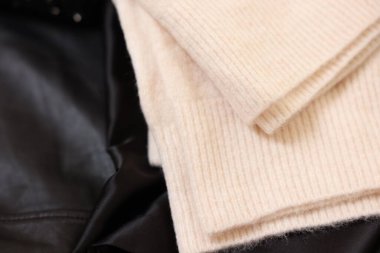 Siyah kumaşta yumuşak bej süveter, üst görünümde.