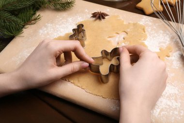 Ahşap masada kesicilerle Noel kurabiyesi yapan kadın, yakın plan.