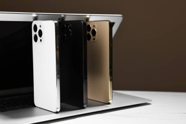 Modern dizüstü bilgisayar ve akıllı telefonlar beyaz masada, kahverengi arka planda, yakın plan. Metin için boşluk