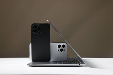 Modern dizüstü bilgisayar ve akıllı telefonlar beyaz masada, kahverengi arka planda. Metin için boşluk